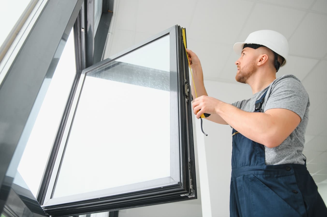 Instalador de ventanas midiendo un marco de ventana con una cinta métrica.